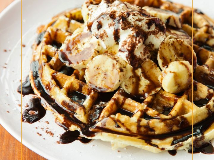 waffles on a plate topped with whipped cream, bananas and chocolate syrup.
