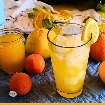 glass of citrus squash on a table surrounded by citrus fruit