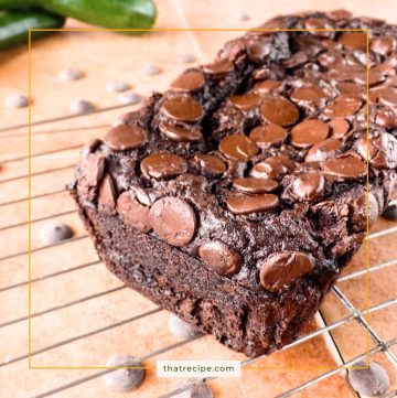 chocolate zucchini bread on a rack with fresh zucchini and chocolate chips