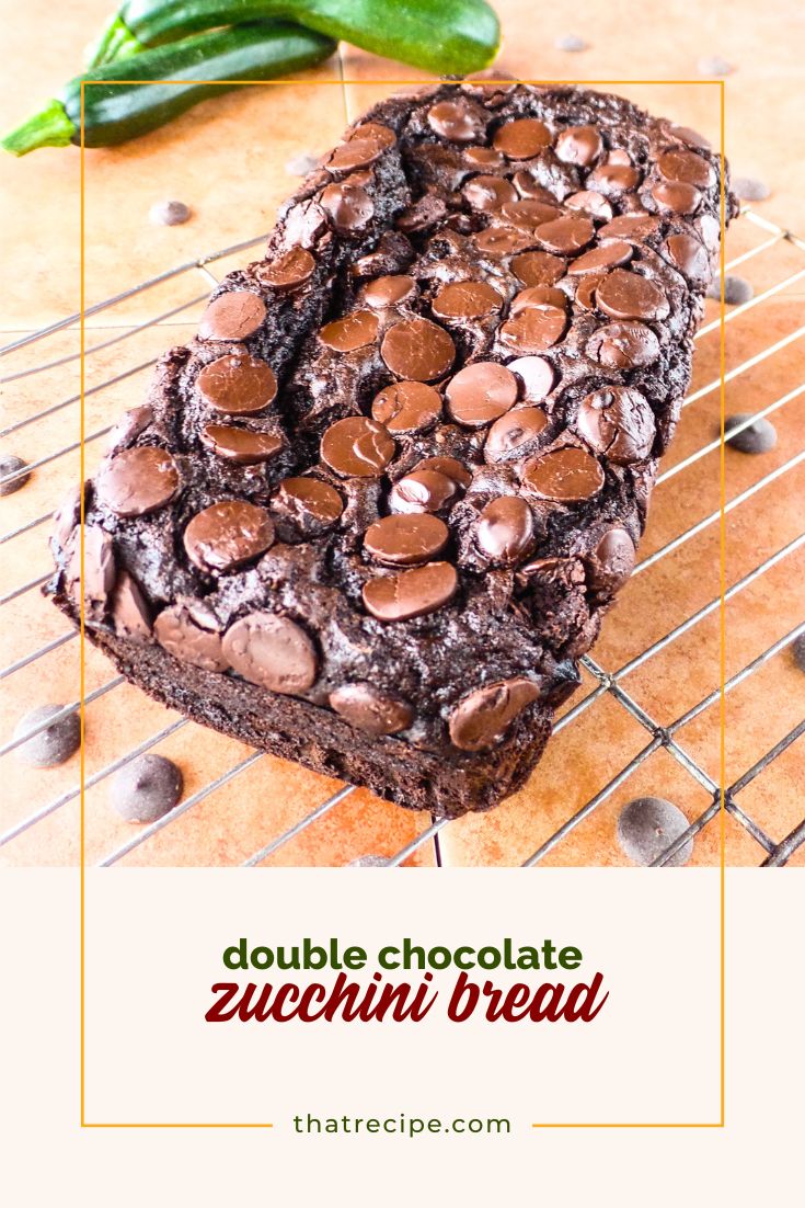 chocolate zucchini bread on a rack with fresh zucchini and chocolate chips