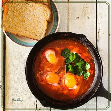 cast iron skillet with eggs in tomato sauce and text overlay "eggs in purgatory"