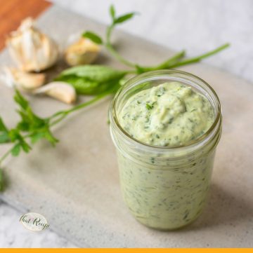 jar filled with green goddess salad dressing on a table with herbs and garlic