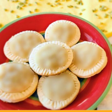 Cookies with a light green glaze on a plate with text overlay Tortitas de Santa Clara