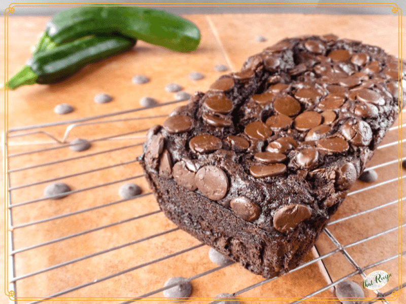 chocolate zucchini bread on a rack with fresh zucchini and chocolate chips